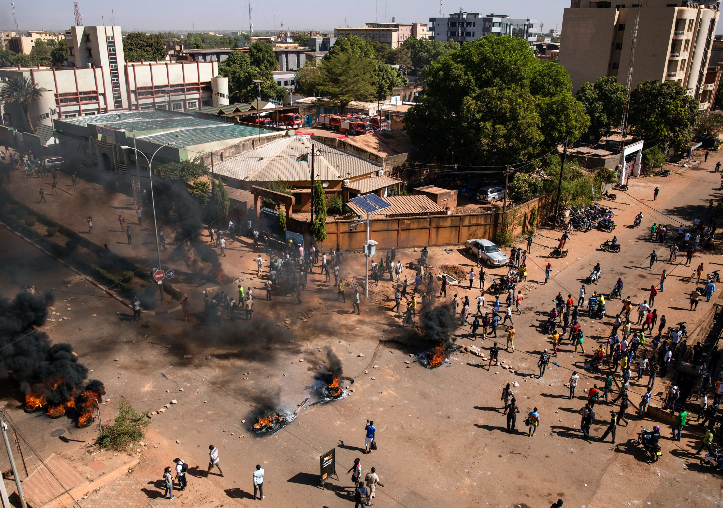 drone view of a city block with people standing near multiple fires burning in the streets after a protest